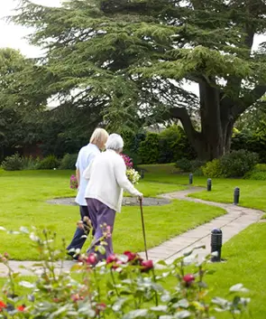 care worker walking with an elderly person in a care home garden