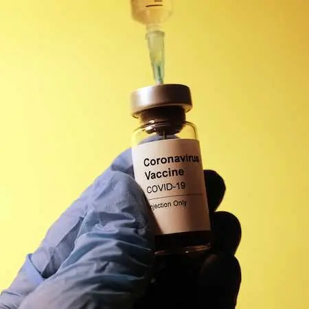 surgical gloved hand holding a coronavirus vaccine vial